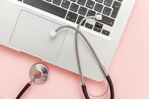 Stethoscope keyboard laptop computer isolated on pink background. Modern medical Information technology and sofware advances concept. Computer and gadget diagnostics and repair photo