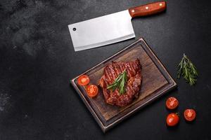 Grilled ribeye beef steak, herbs and spices on a dark table photo