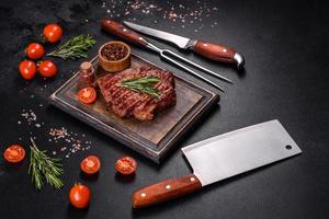 Grilled ribeye beef steak, herbs and spices on a dark table photo