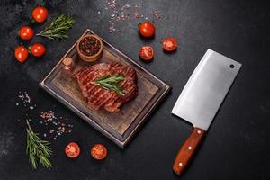 Grilled ribeye beef steak, herbs and spices on a dark table photo