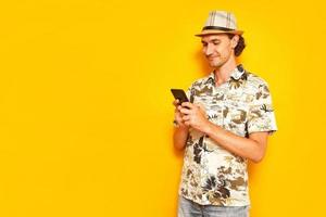 male tourist traveler is holding phone in his hands, texting on smartphone with family friends, smiling isolated on yellow background with space for text. concept - people, communication, technology photo