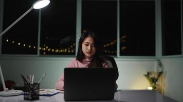 femme asiatique carrière indépendante portant des vêtements roses faisant de la paperasse il y a un ordinateur portable sur la table. et des lanternes allumées, restant délibérément à la maison pendant le gallois la nuit video