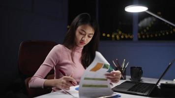 mulher freelance asiática usa roupas cor de rosa enquanto trabalha demais. escreva com laptop na mesa e lâmpada em casa à noite. conceito freelance pessoas trabalham ao longo do tempo. video