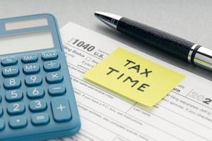 concepto de tiempo de impuestos. nota amarilla con mensaje, formulario de impuestos, calculadora y bolígrafo en la mesa
