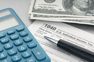 concepto de impuestos. formulario de impuestos, calculadora, dinero y bolígrafo en la mesa foto