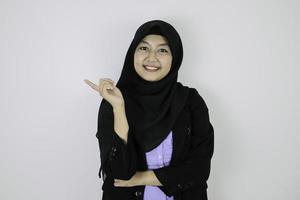 feliz joven islámica asiática con pañuelo en la cabeza sonríe y señala al lado. foto