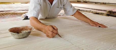 la mano con un lápiz hace marcas en la alfombra. tejido y fabricación de alfombras artesanales foto