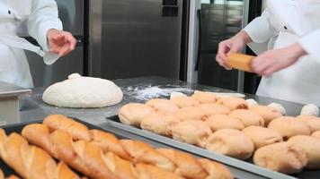 Close up of chefs' hand in white cook uniforms and aprons are kneading raw pastry dough, preparing bread, cakes, cakes, and fresh bakery food, baking in oven at stainless steel kitchen of restaurant. video