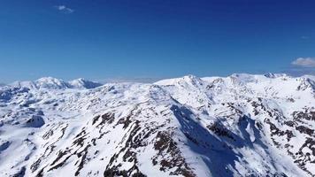 flygdrönare av en fantastisk panoramautsikt över en bergskedja täckt med snö under en solig dag. vintersäsong och semester i bergen. blå himmel och vita livfulla färger. filmisk tagning. video