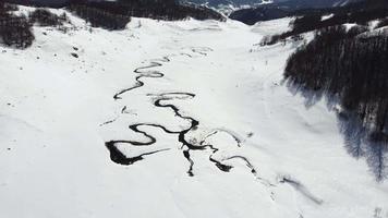 Amazing aerial view of a swirly river in the mountains during winter sunny day. Everything is white and covered with snow. Beautiful winter travel destination. video