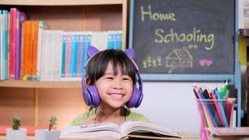 Cute little girl with headphones listening to audiobooks and looking at English learning books on the table. Learning English and modern education video