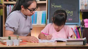 menina asiática estuda em casa durante a quarentena com a mãe. mãe ajudando a filha com lição de casa em casa. Educação escolar em casa. video