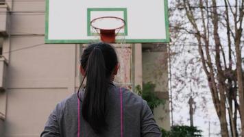 aziatische vrouw die basketbal houdt die camera bekijkt bij openluchtbasketbalspeelplaats. video