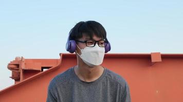 feliz jovem asiático usando uma máscara e fones de ouvido ouvindo música no jardim de verão.