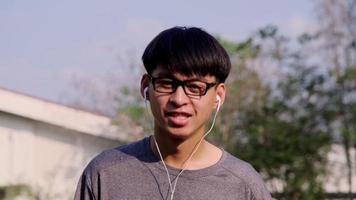 feliz jovem asiático usando fone de ouvido ouvindo música no jardim de verão. video