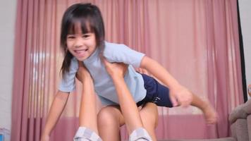 Happy children playing with mom at home. Mother lies on the warm floor and lifts up her little daughter, imagining herself as an airplane enjoying flying in the air. video