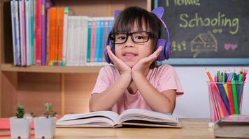 Cute little girl with headphones listening to audio books with english learning books on the table. Learning English and modern education video