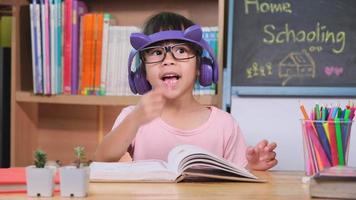 linda niña con auriculares escuchando audiolibros y mirando libros en casa. aprender inglés y educación moderna video