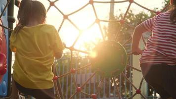 felici due bambine che si arrampicano sulla rete di corda al parco giochi. bambine attive nel parco giochi all'aperto. sana attività estiva per i bambini. video