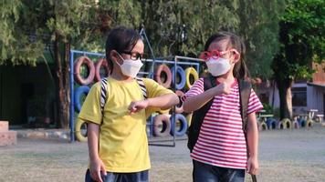 New Normal greeting. Children wearing disposable masks and bumping elbows greet each other at school. Back to school concept video