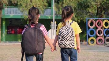 twee schattige schoolmeisjes die zomerkleren dragen met rugzakken die samen op school lopen, achteraanzicht. terug naar school concept video