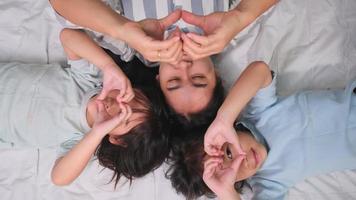 Top view portrait of Happy children playing with their mother lying on a bed at home and looking at the camera. Good time at home. video