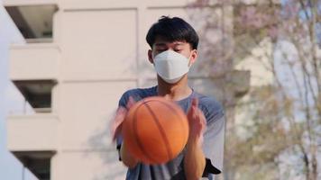 joven atlético asiático jugando baloncesto al aire libre. jóvenes deportistas practicando baloncesto en la cancha al aire libre.