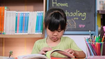 schattig klein meisje dat thuis een boek leest tijdens quarantaine. nieuw normaal. thuisonderwijs. video