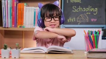 Cute little girl with headphones listening to audio books with english learning books on the table. Learning English and modern education video