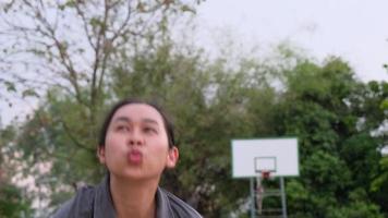 Asian female athlete wearing headphones poses with basketball at outdoor basketball court. video