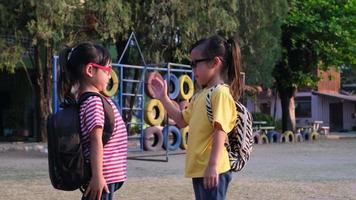 twee schattige schoolmeisjes die een zomeroutfit met rugzakken dragen en hallo vijf geven op school. terug naar school concept video
