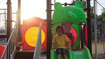 niños asiáticos felices jugando juntos en el patio de recreo. niña activa en el patio de recreo al aire libre. Actividad de verano saludable para niños. video