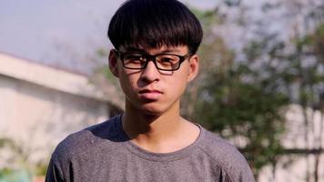 Portrait of a confident young man in glasses and casual gray t-shirt standing in a summer garden. video