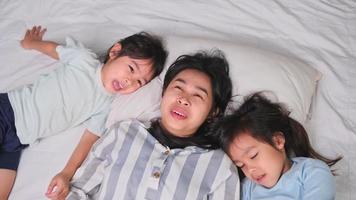 Top view portrait of Happy children playing with their mother lying on a bed at home and looking at the camera. Good time at home. video