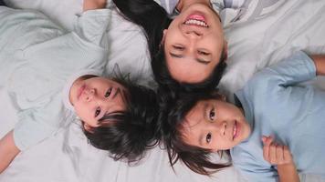 Top view portrait of Happy children playing with their mother lying on a bed at home and looking at the camera. Good time at home. video