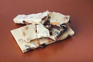 white chocolate with nuts, raisins on a brown background photo