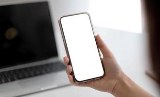 vista recortada de manos de mujer sosteniendo un teléfono inteligente con pantalla de espacio en blanco para su mensaje de texto o contenido de información, mensaje de texto de lectura femenina en el teléfono celular durante la oficina. foto