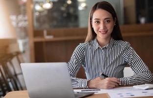 Charming asian businesswoman sitting working on laptop in office. photo