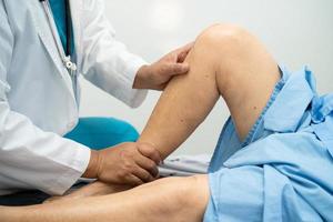 médico asiático fisioterapeuta que examina, masajea y trata la rodilla y la pierna del paciente mayor en el hospital de enfermería de la clínica médica ortopedista. foto