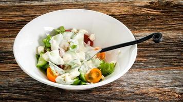 Vegetables salad with dressing inside white bowl on rustic table photo