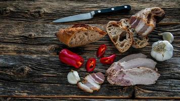 Old rustic wooden table with bread, meat, bacon, red pepper and garlic from above photo