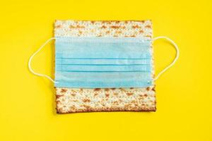 Traditional Jewish bread matzo and medical mask on a yellow background. Passover concept during the coronavirus pandemic.