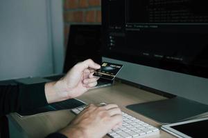 Hacker in the hood working with computer and holding credit card with payment hacking concept. photo