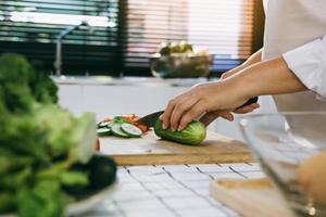 Housewife using knife and hands cutting cucumber on wooden board in kitchen room. photo