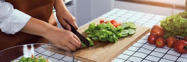 Asian woman uses a knife to cut the salad greens in the kitchen.
