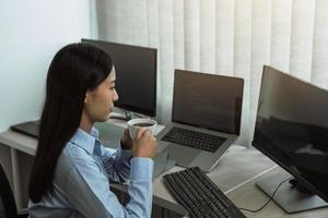una mujer asiática estaba tomando café temprano en la mañana mientras contemplaba el programa y el código en la pantalla de la computadora. foto