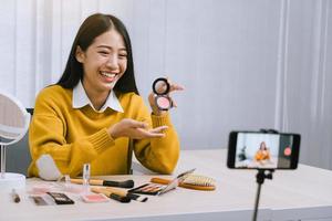 Beautiful asian woman blogger using camera phone recording vlog video live streaming and showing how to make up cosmetics at home.