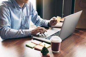 Young asian man typing laptop keyboard and holding credit card at home with online shopping or internet banking concept. photo