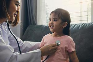 Confident asian woman healthcare professional visit her patient using a stethoscope during a young female patient well check at home. photo