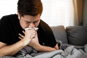 los asiáticos están enfermos o enfermos de bronquitis mientras tosen cubriéndose la boca con papel de seda cuando se sientan en el sofá de casa. foto